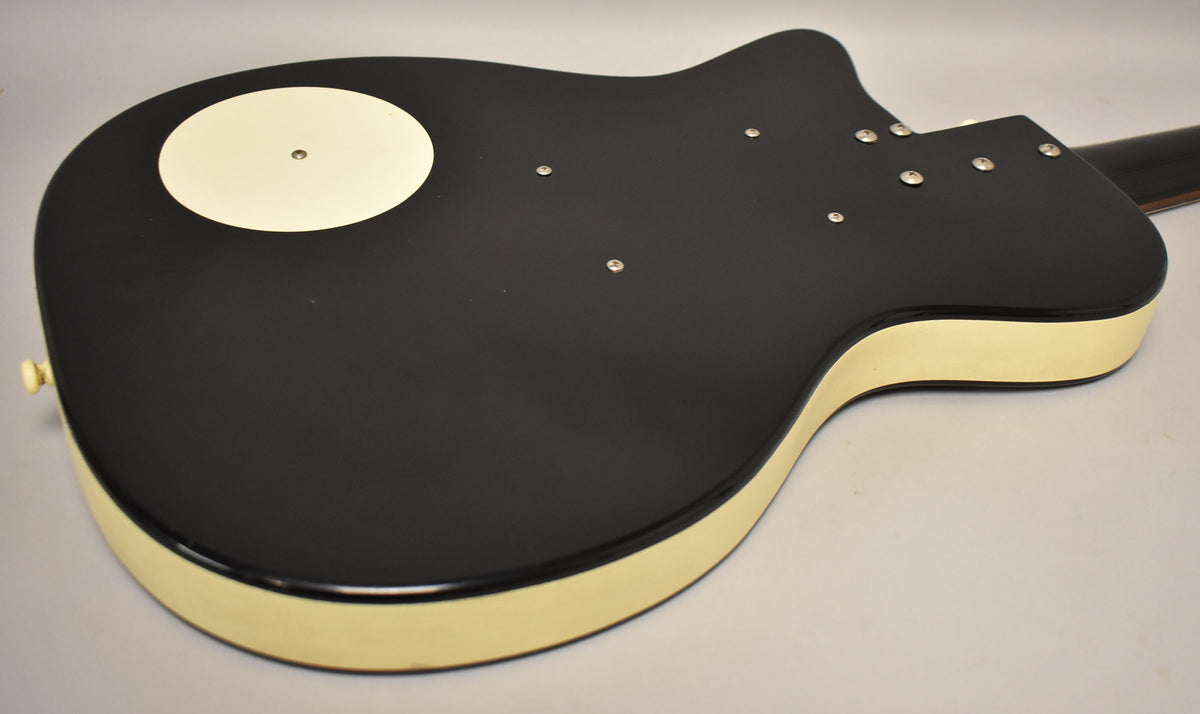 The guitar's black back with cream sides is angled, showing a circular cream cover and six chrome screws near the neck joint.