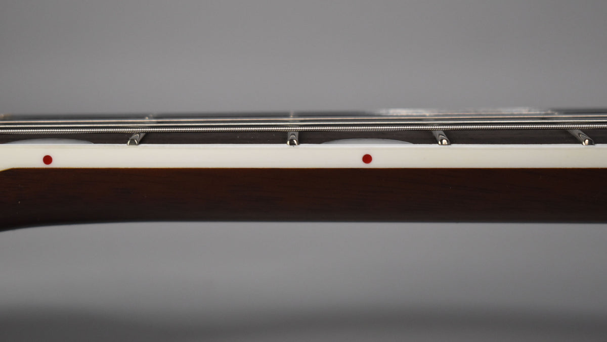Close-up of the dark brown fretboard's side, showing white binding with red dot markers and silver frets and strings.