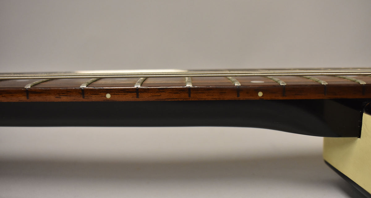 Close-up of the guitar's dark brown fretboard with silver frets and white dot inlays, showing light wear and a black neck.