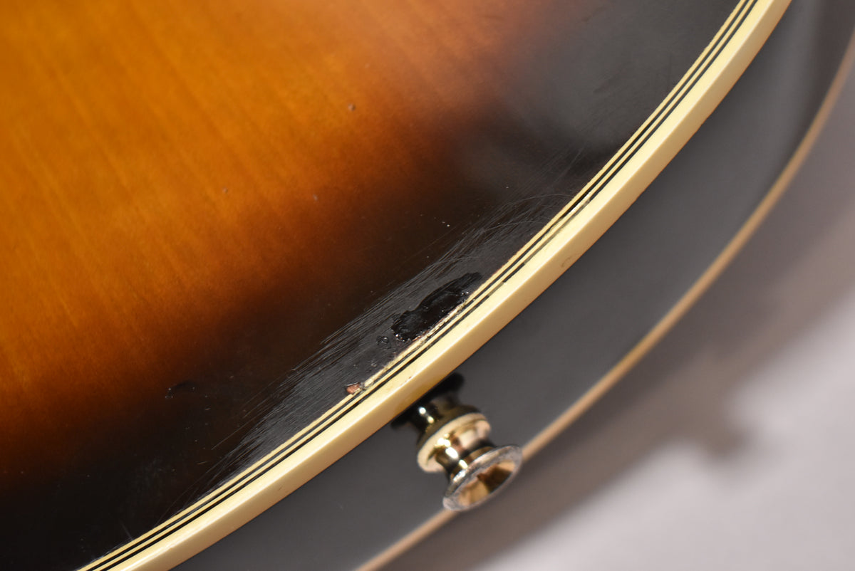 Close-up of the lower bout, showing the tobacco sunburst finish with heavy scratches and a chip, and a gold strap button.