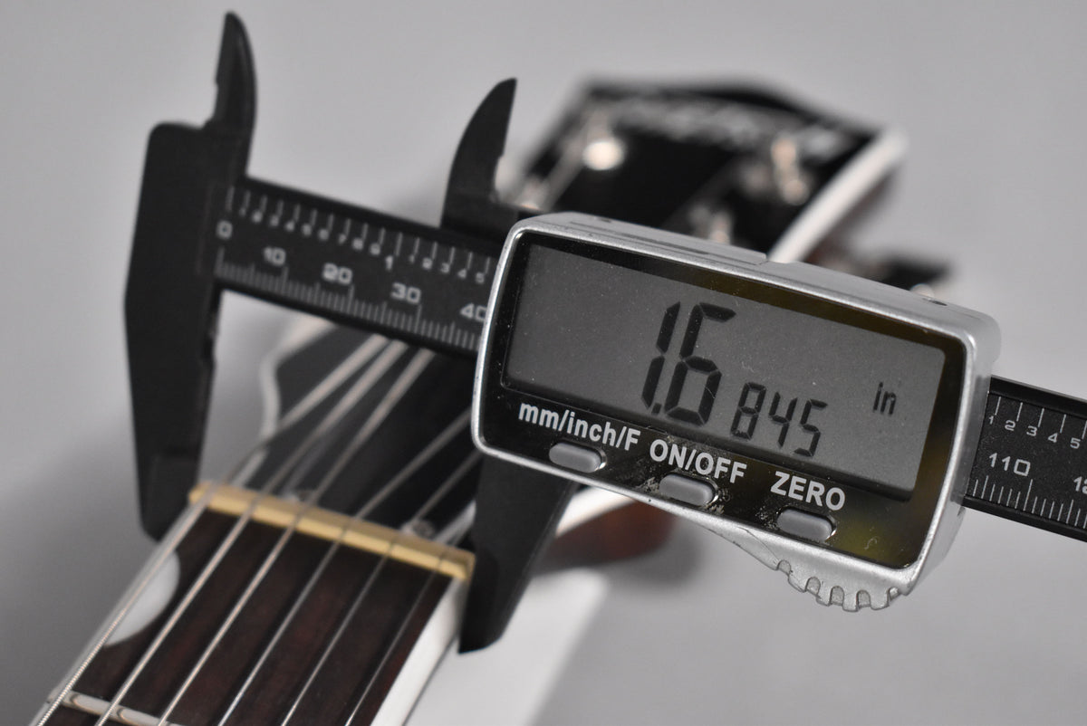 A digital caliper measures the guitar's nut width at 1.6845 inches, with the dark fretboard and light nut visible.