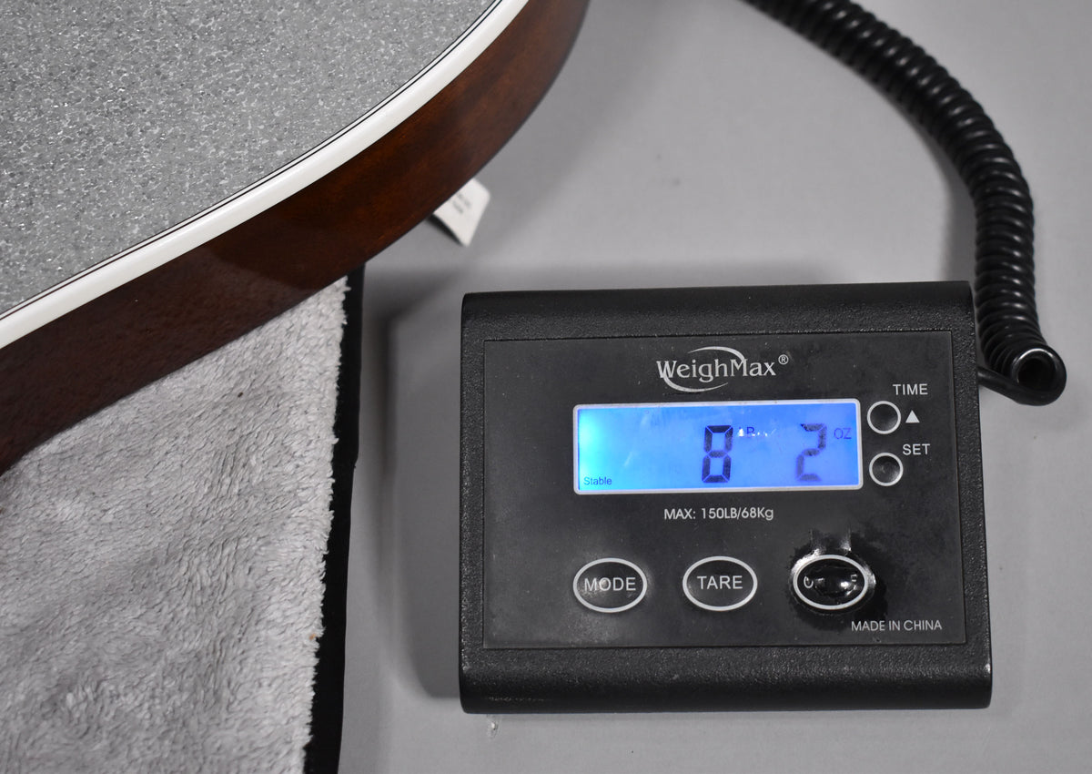 The guitar's lower bout, with dark wood sides and white binding, rests on a grey towel next to a digital scale displaying "8 lb 2 oz".