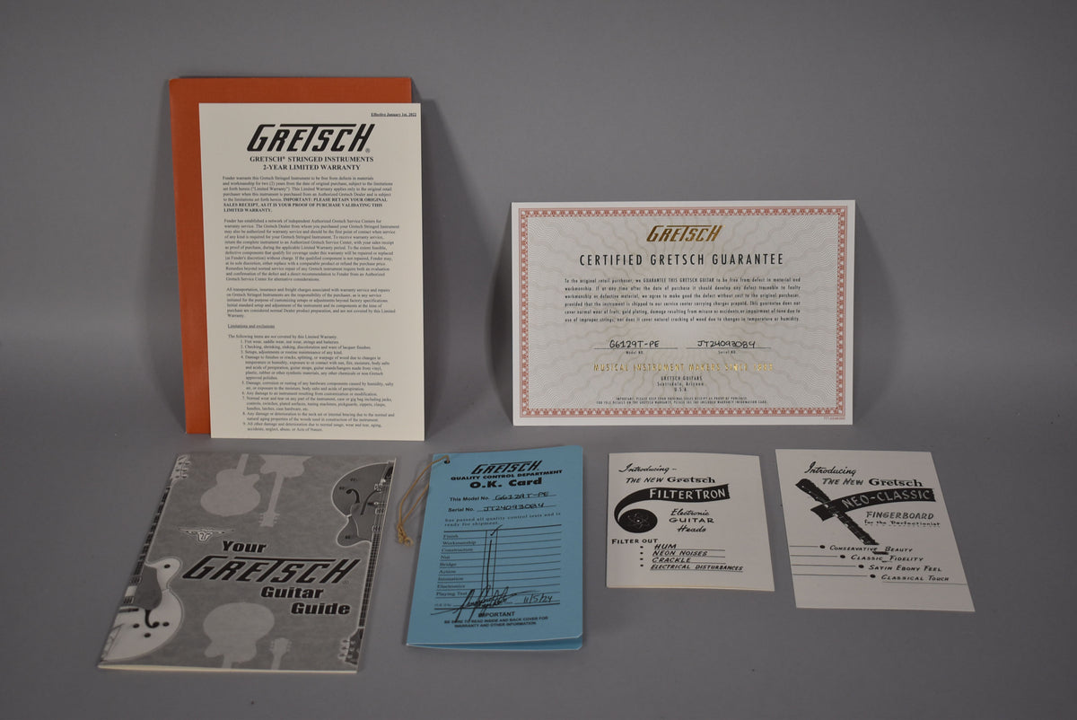 A top-down view of the guitar's paperwork, including a warranty, guarantee, guitar guide, O.K. card, and two product feature cards.