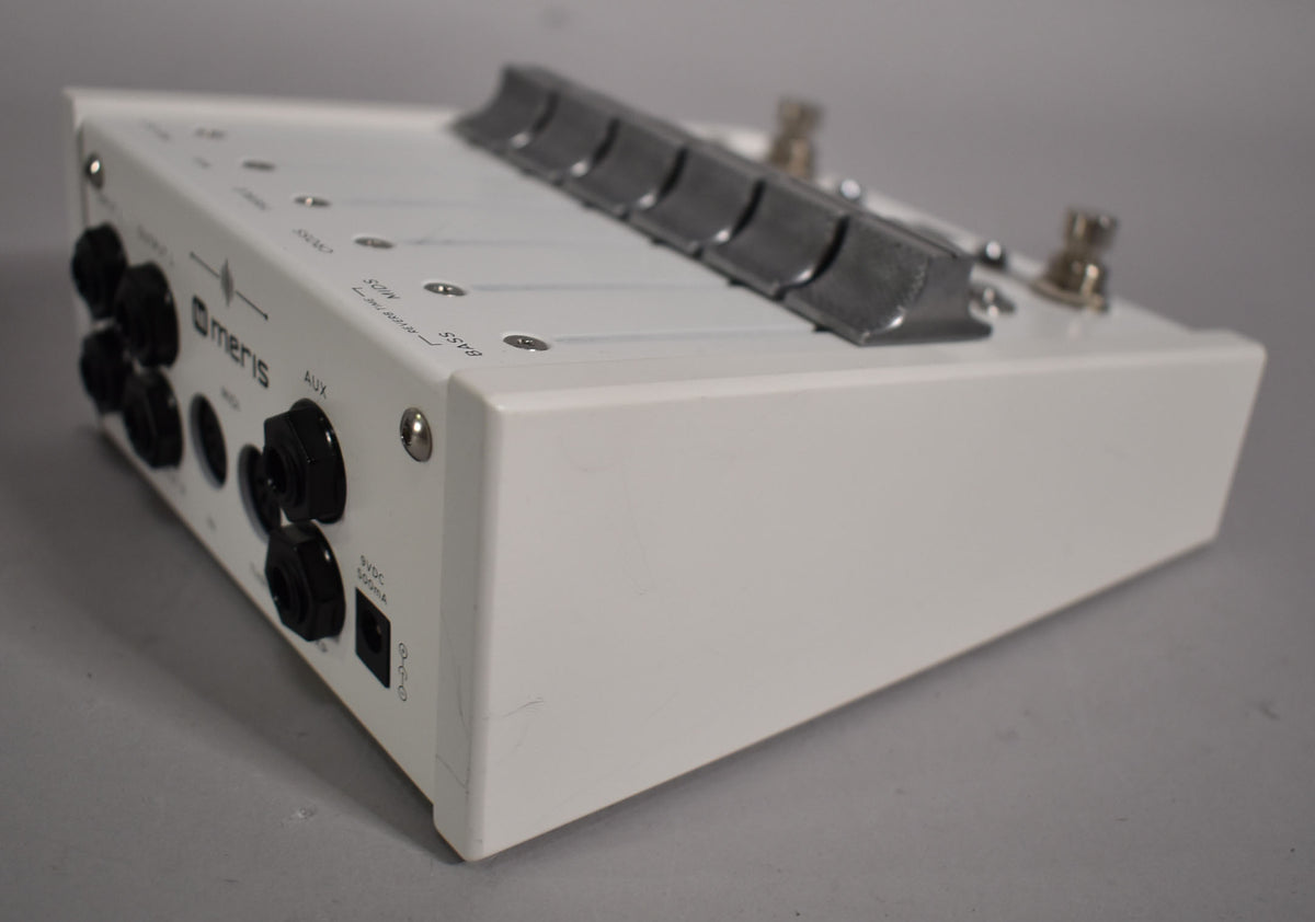 Angled view of the white pedal, showing the left side with several black jacks and knobs, and the top with six metal sliders.
