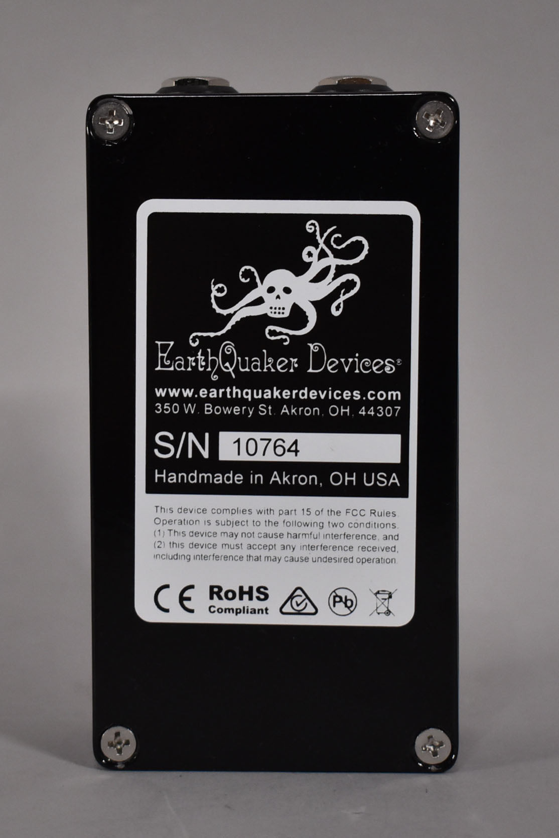 The pedal's black bottom plate is centered, showing a white label with an octopus skull logo and serial number 10764.