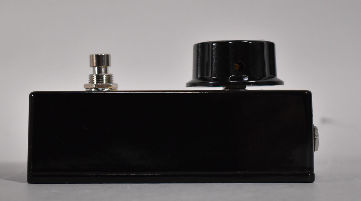 The black pedal is viewed from the right side, showing a silver footswitch, a large black control knob, and a silver jack.