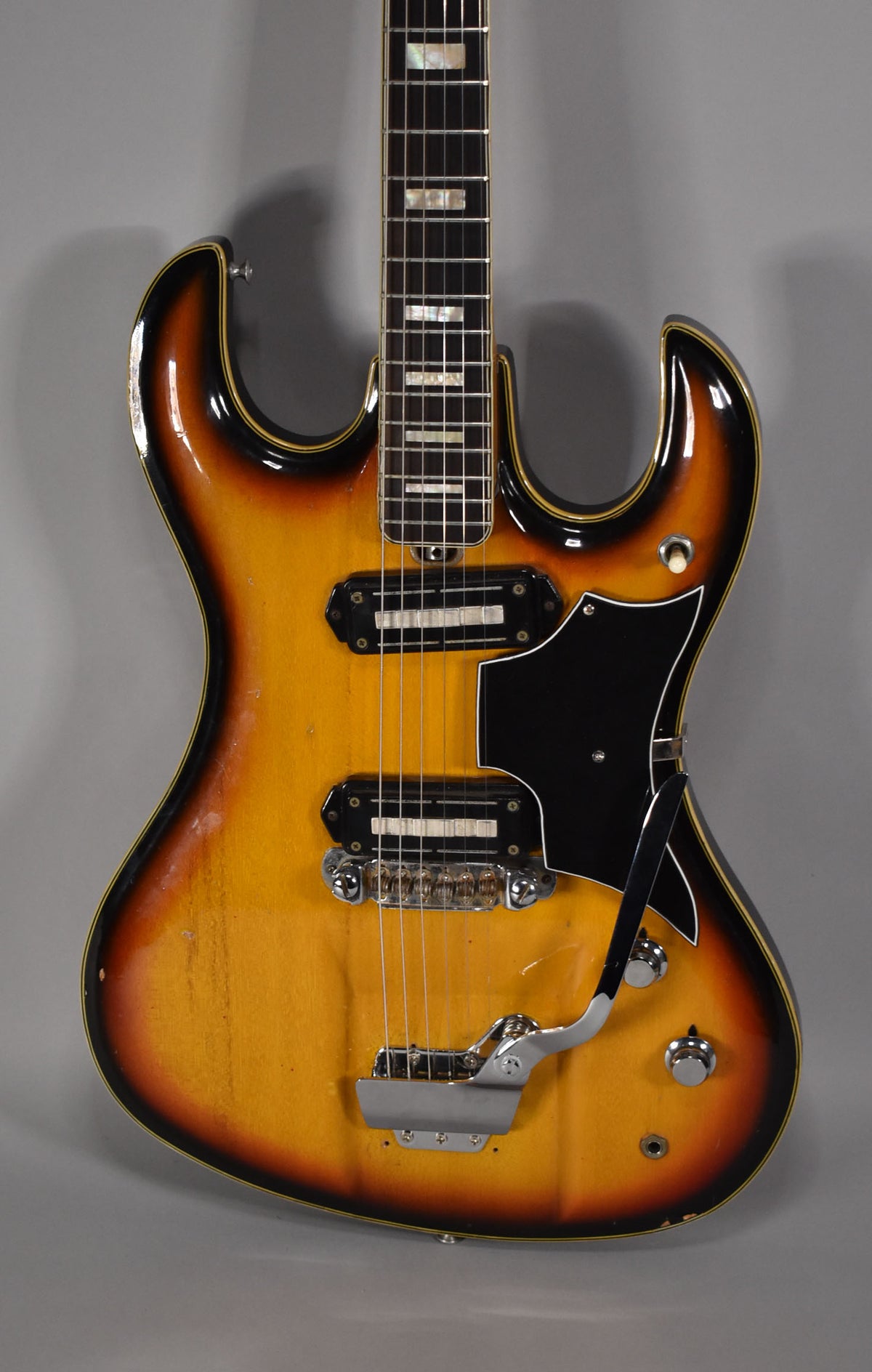The sunburst guitar body is framed from the neck to the lower bout, showing two pickups, a black pickguard, and a tremolo arm.