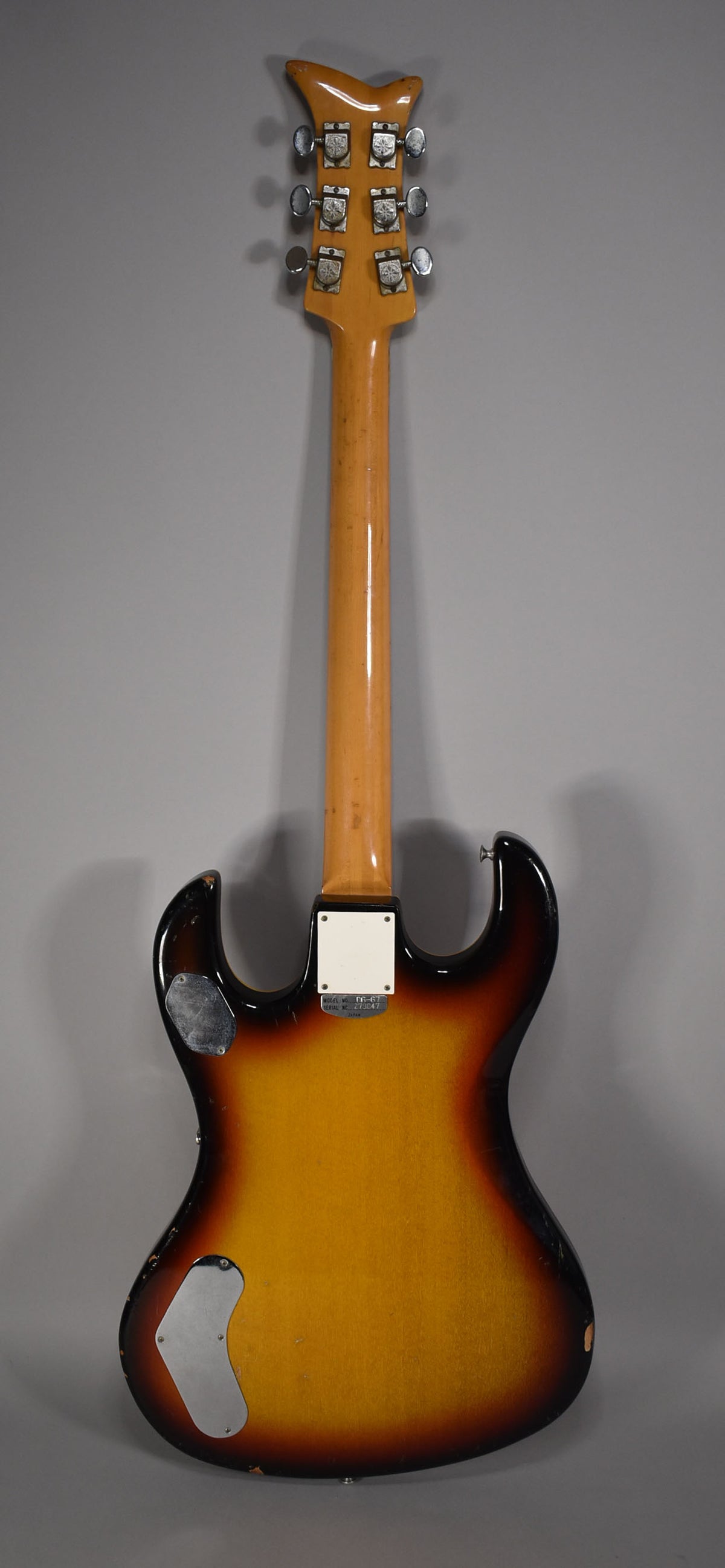 Rear view of a sunburst guitar with a light-colored neck, six tuners, and two metal control plates on the body.
