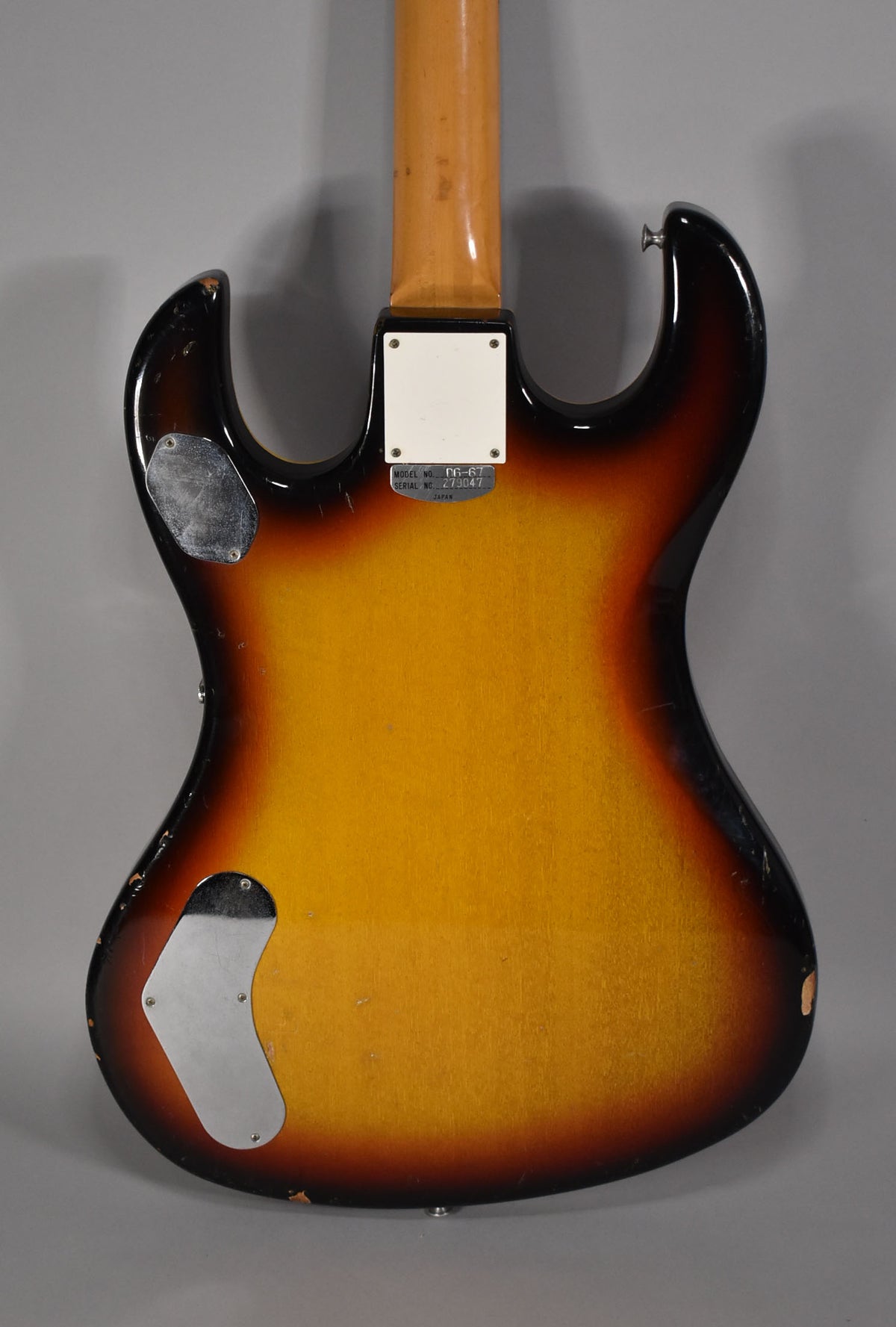 Rear view of a sunburst electric guitar body with a maple neck, two chrome control plates, and visible finish wear.