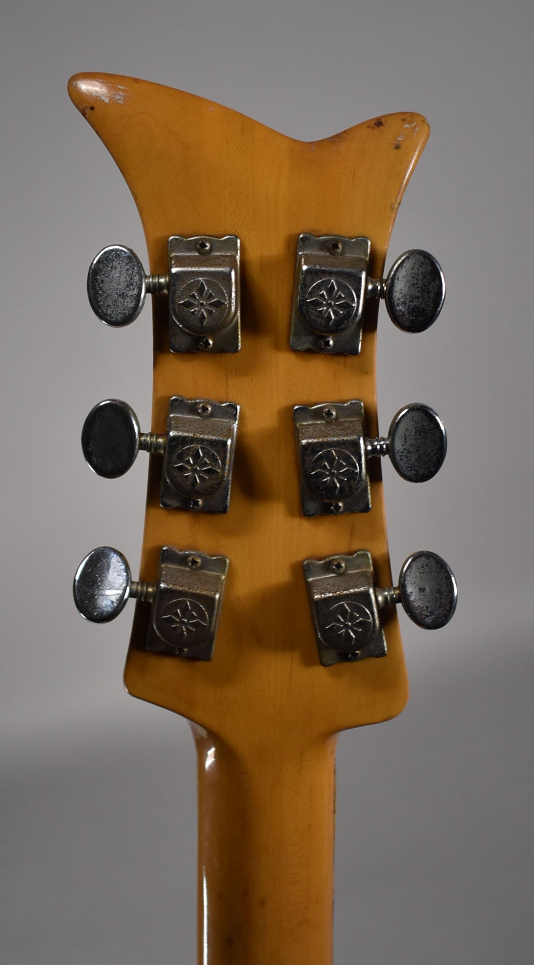 Rear view of the guitar's headstock and top of the neck, showing six chrome tuners with starburst emblems and wear on the headstock edges.