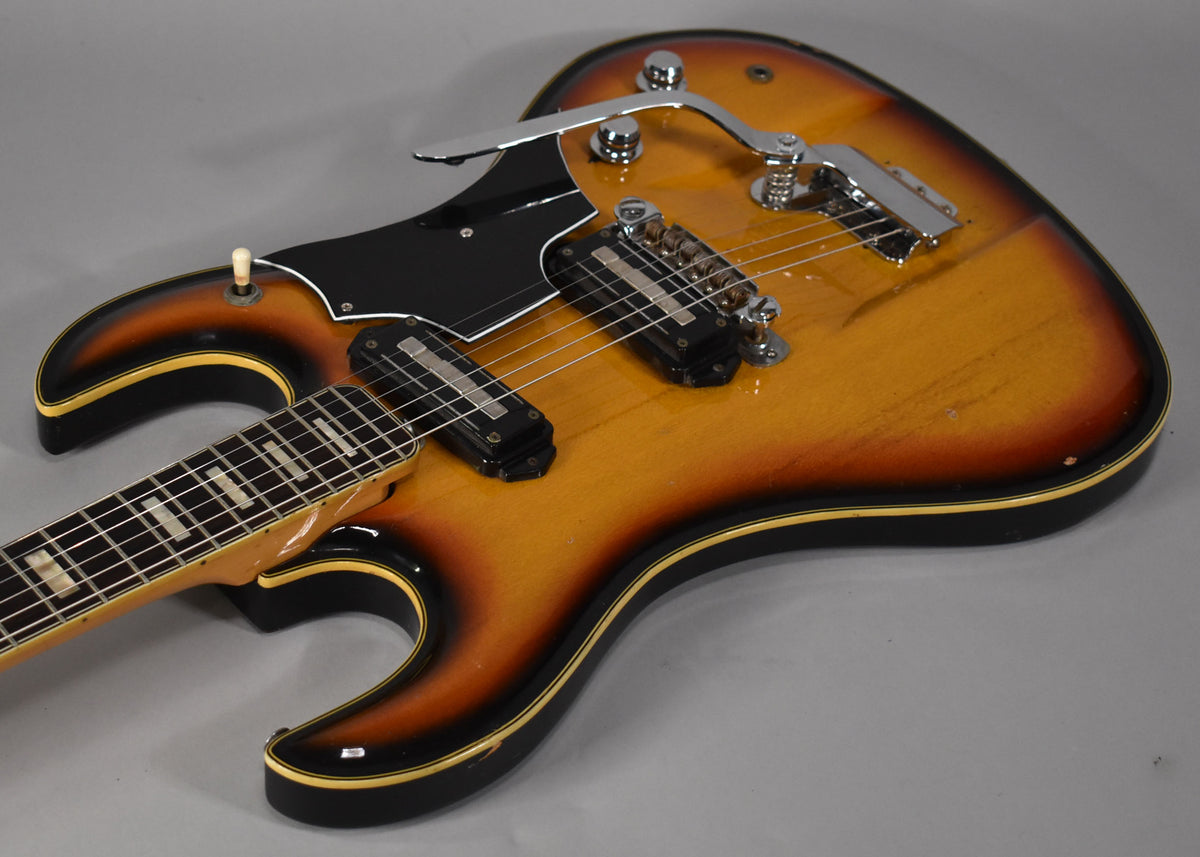 Angled view of a sunburst electric guitar with two pickups, a black pickguard, and a chrome tremolo system.