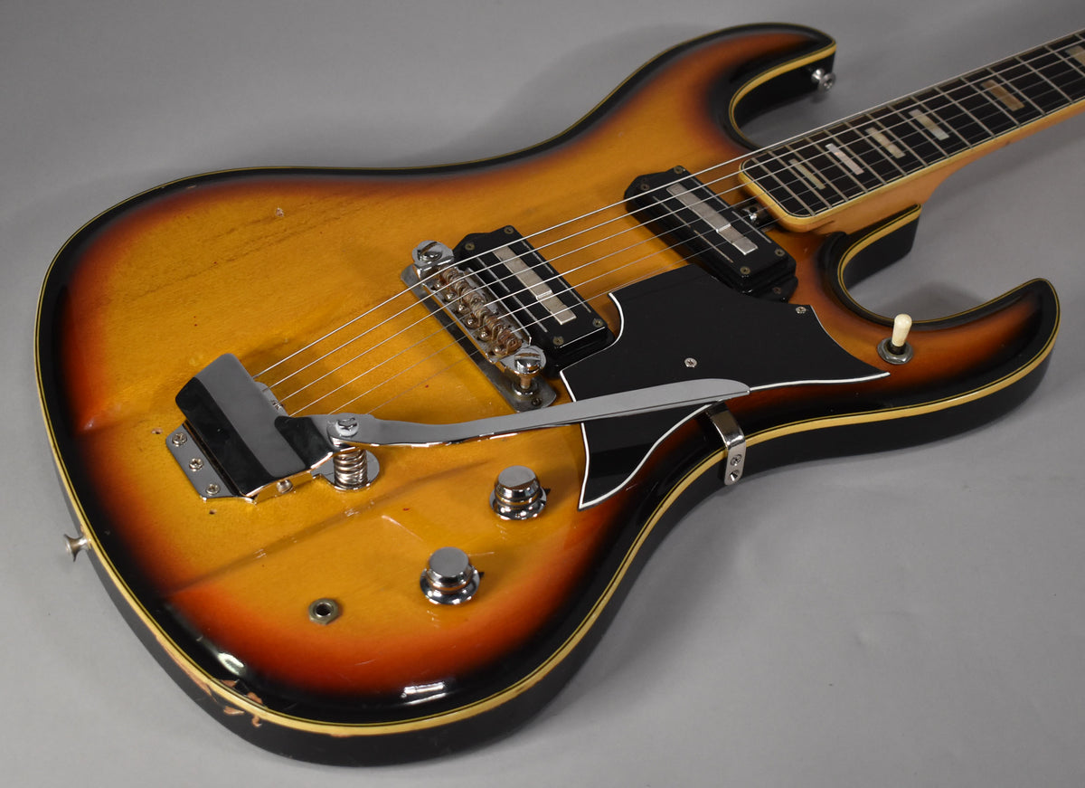 The guitar's sunburst body, with a black pickguard and chrome hardware, shows visible finish wear and checking.