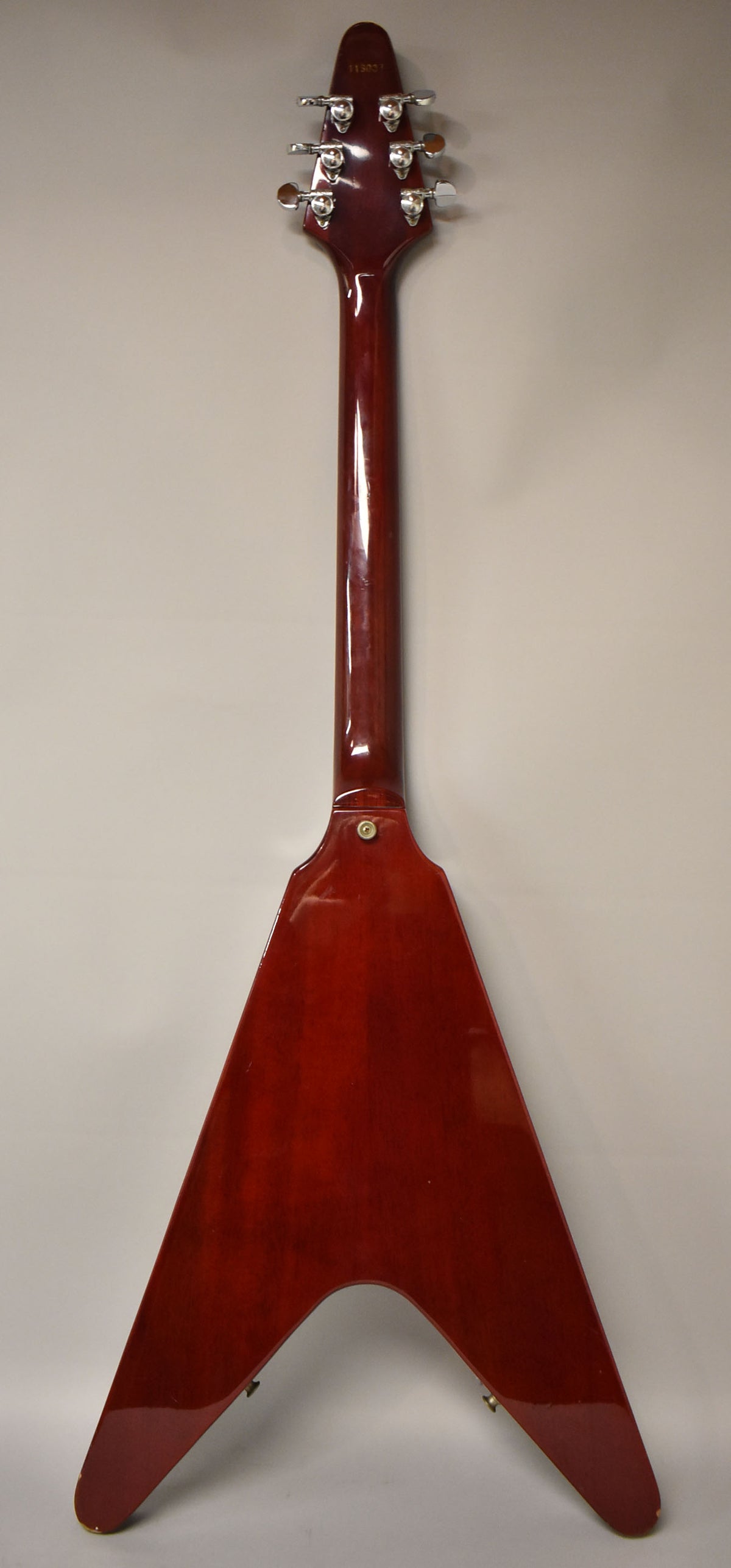 Full back view of the cherry red Flying V, showing the glossy finish, chrome tuners, and a small chip on the lower left wing.