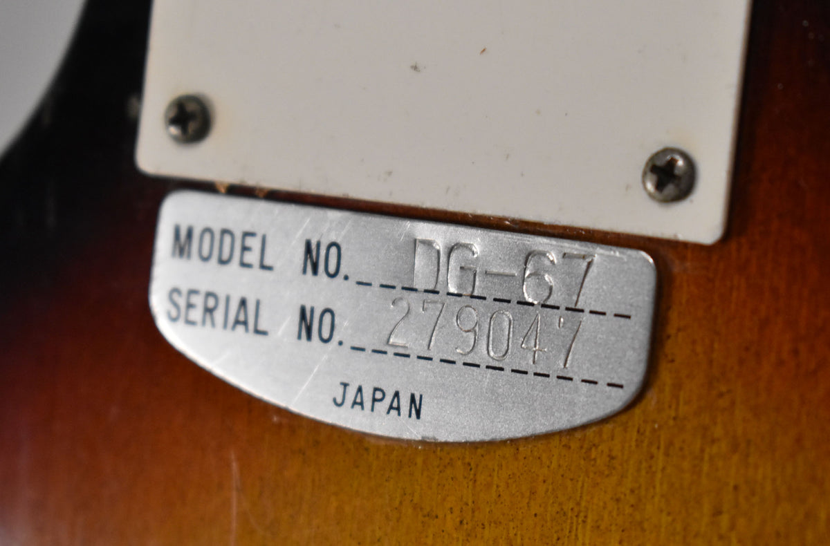 Close-up of the guitar's sunburst body, showing a metal plate with "MODEL NO. DG-67" and "SERIAL NO. 279047 JAPAN" stamped on it.