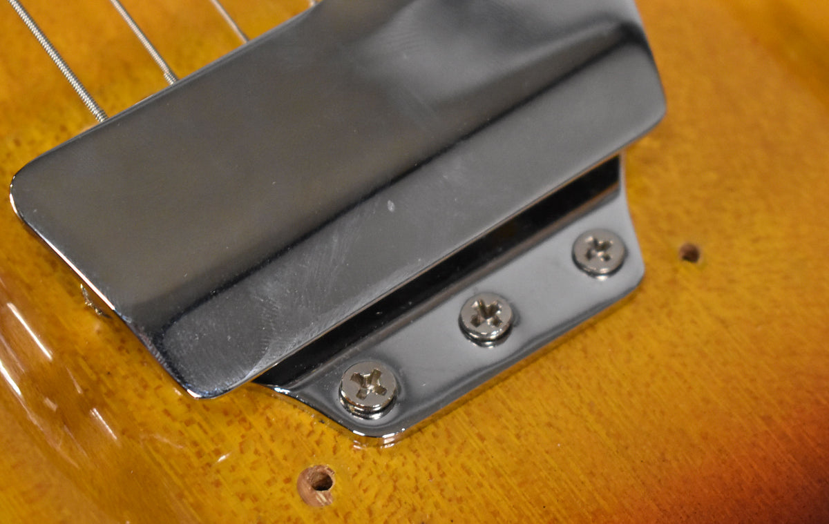 Close-up of the guitar's chrome bridge cover, showing three mounting screws, light scratches, and two empty screw holes on the sunburst body.