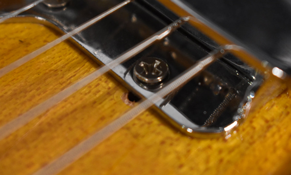 Close-up of the guitar's bridge pickup, showing the chrome cover, a mounting screw, and four strings over the sunburst body.