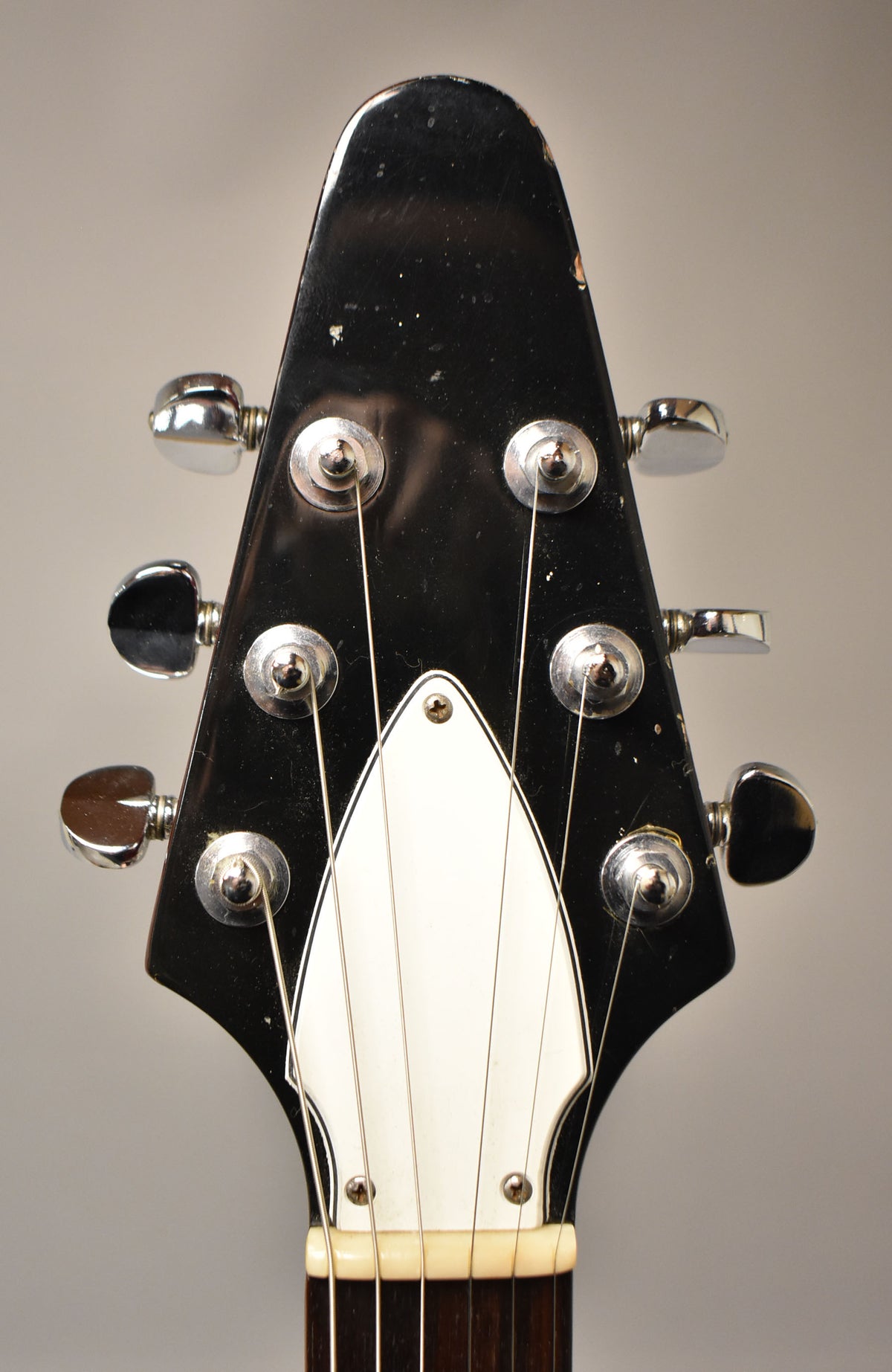 Close-up of the black headstock with chrome tuners, showing a white truss rod cover and visible wear and scratches.