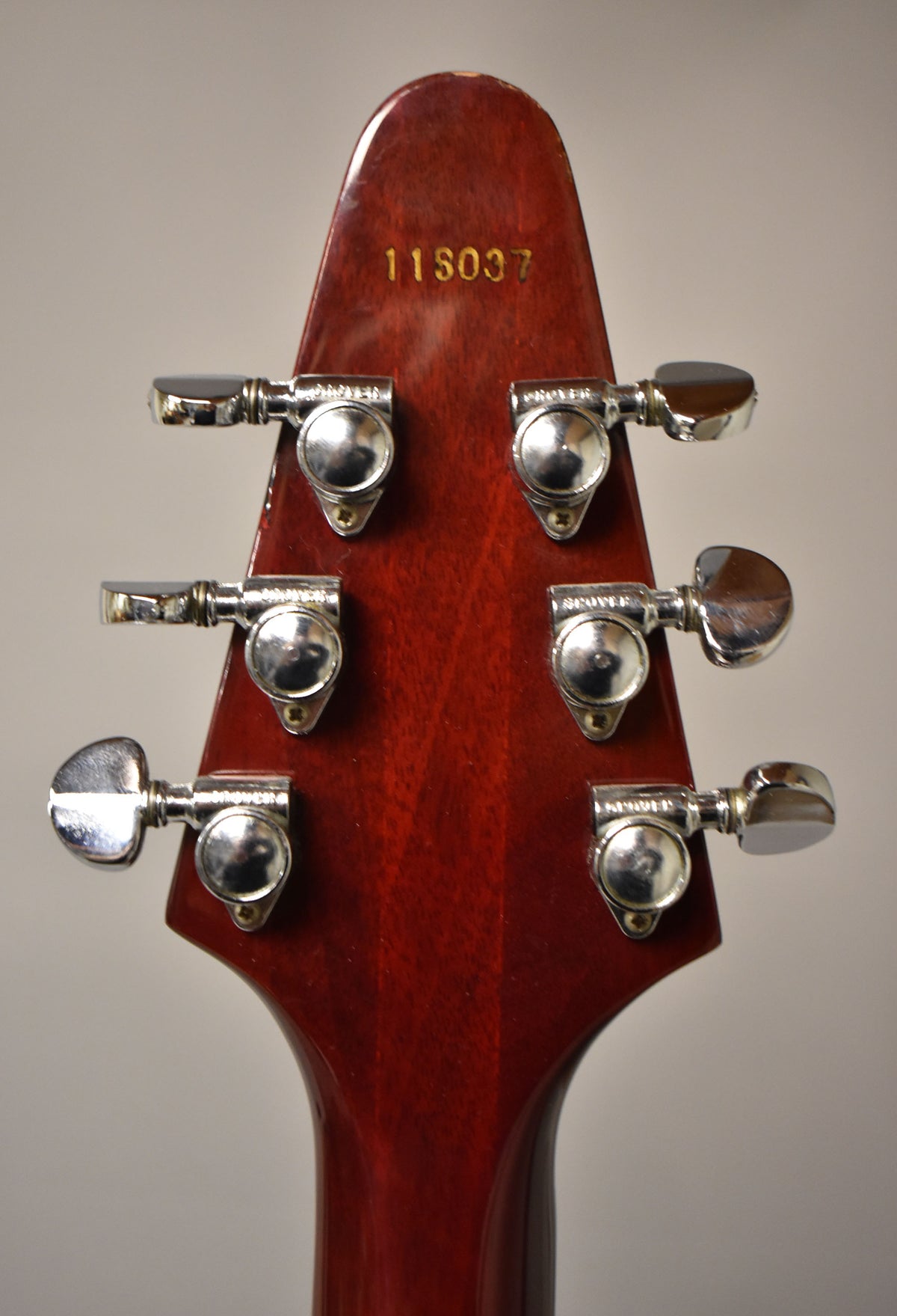 Rear view of the cherry red headstock with six chrome tuners, showing some finish wear and a gold serial number "11S037".