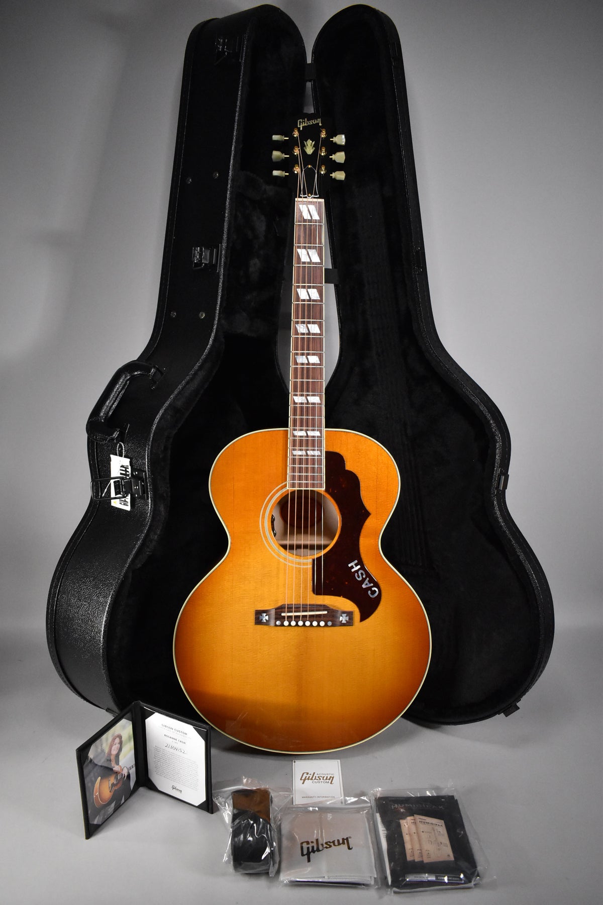 Full-length view of a cherry sunburst acoustic guitar with block inlays, a "CASH" pickguard, and its open hard case.