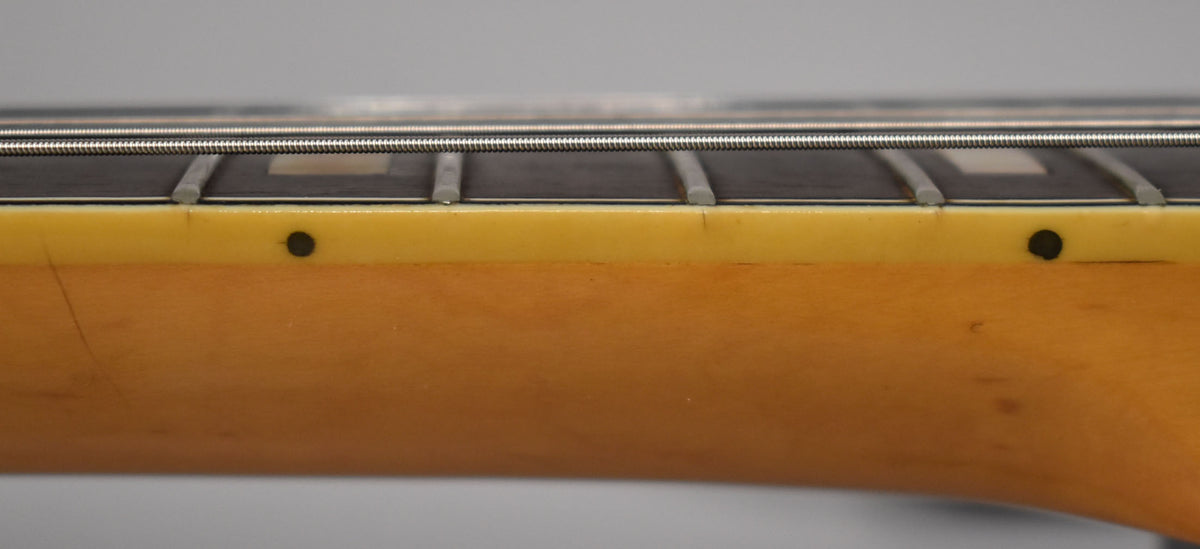 Close-up of the guitar's neck and fretboard, showing dark frets, white rectangular inlays, and two black side dots.