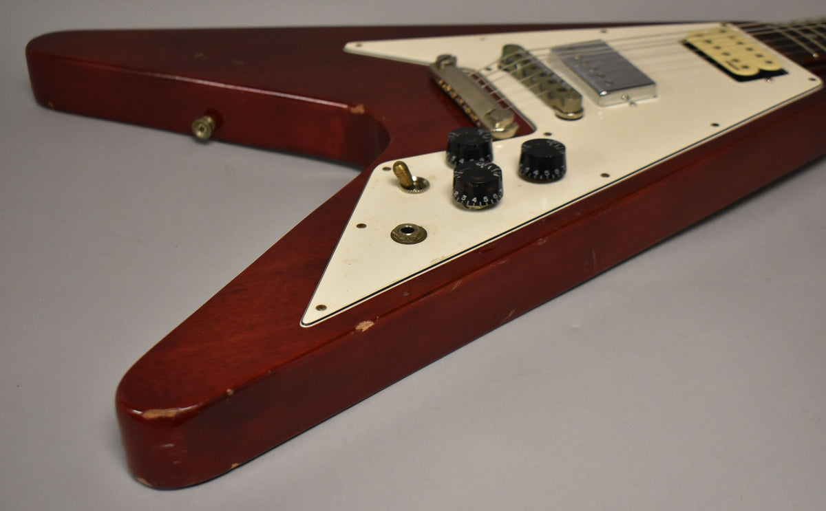 Cherry red Flying V body, angled from the lower bout, showing the cream pickguard, three black knobs, and a chrome bridge.