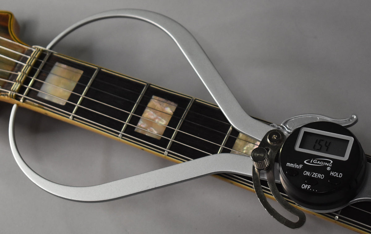 Close-up of the guitar's fretboard with block inlays, showing a digital caliper measuring the fret height at 1.54.