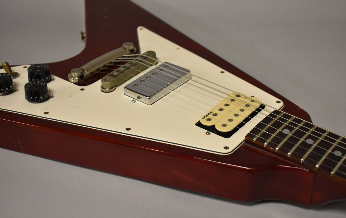 Close-up of the cherry red Flying V's body, showing the cream pickguard, two humbuckers, three black control knobs, and a tune-o-matic bridge.