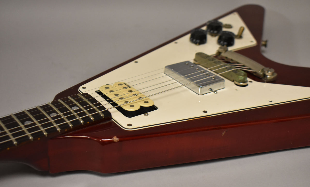 The cherry red Flying V body, with a white pickguard, shows a cream neck humbucker, chrome bridge humbucker, and a tune-o-matic bridge.