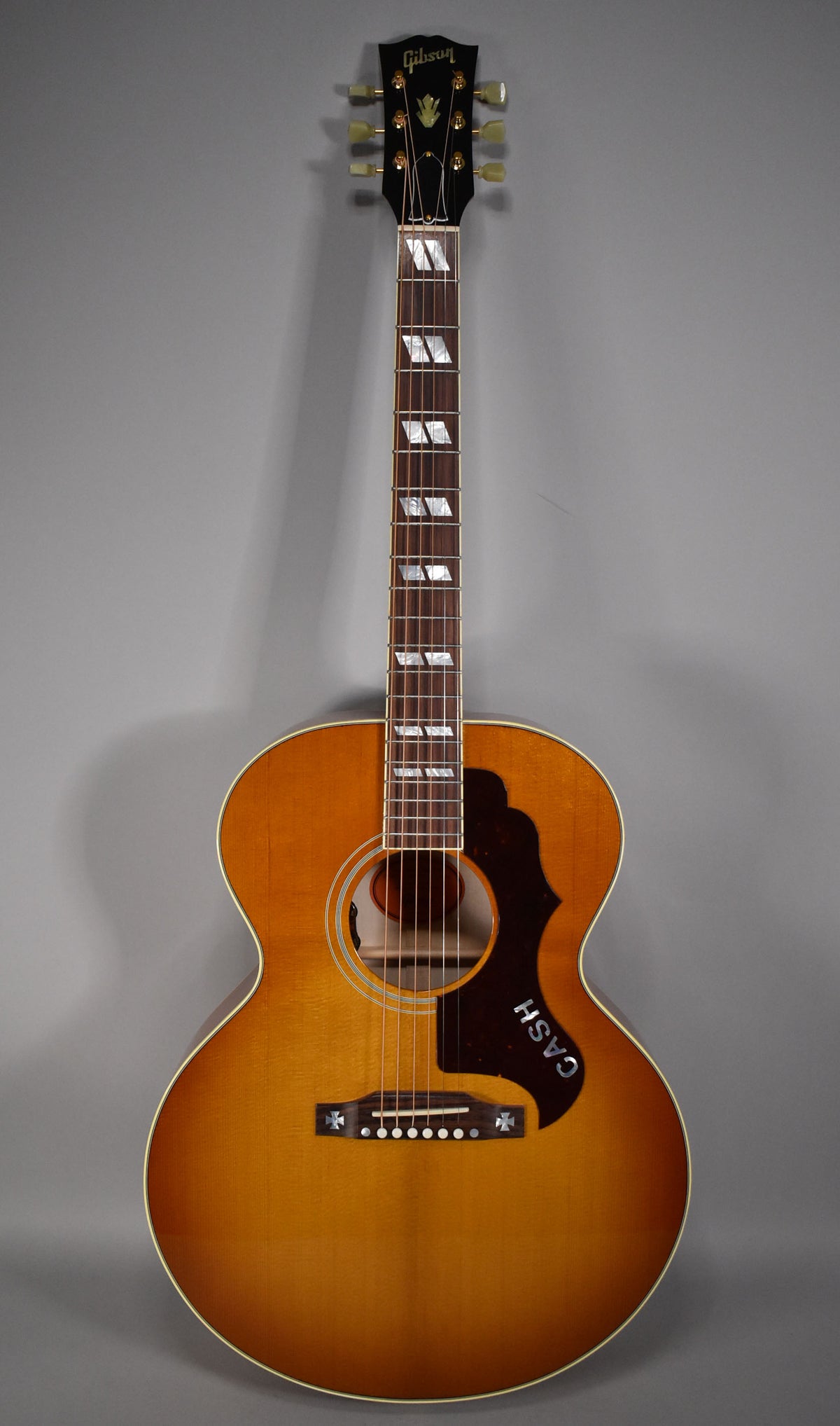 Full front view of the acoustic guitar, showing its cherry sunburst finish, block inlays, and a black pickguard with "CASH" in white.