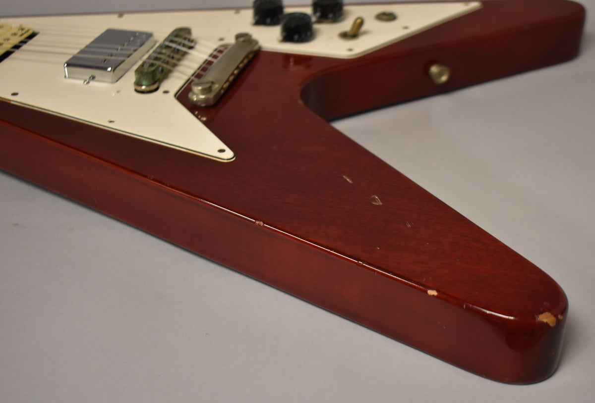 Close-up of the cherry red Flying V body, showing the white pickguard, chrome humbucker, and visible chips on the lower bout.