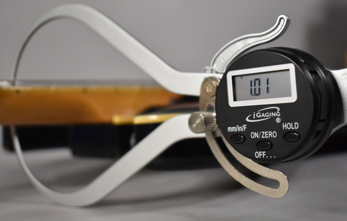 A digital caliper measures the guitar's sunburst body, showing a reading of 1.01, likely indicating thickness.