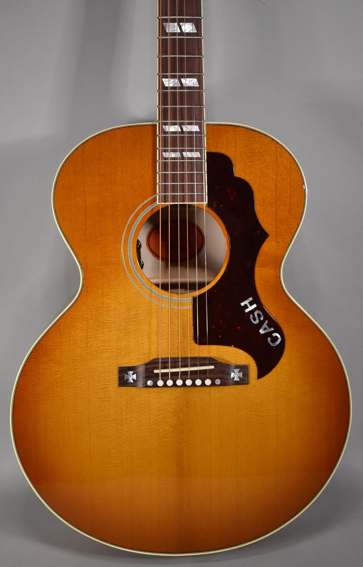 Acoustic guitar with a cherry sunburst finish, "CASH" on the pickguard, and cross inlays on the bridge.