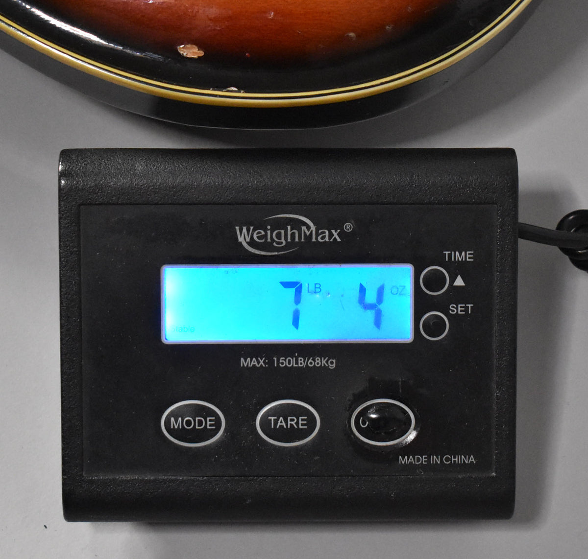 The guitar's sunburst body is partially visible above a black digital scale displaying "7 LB. 4 OZ."