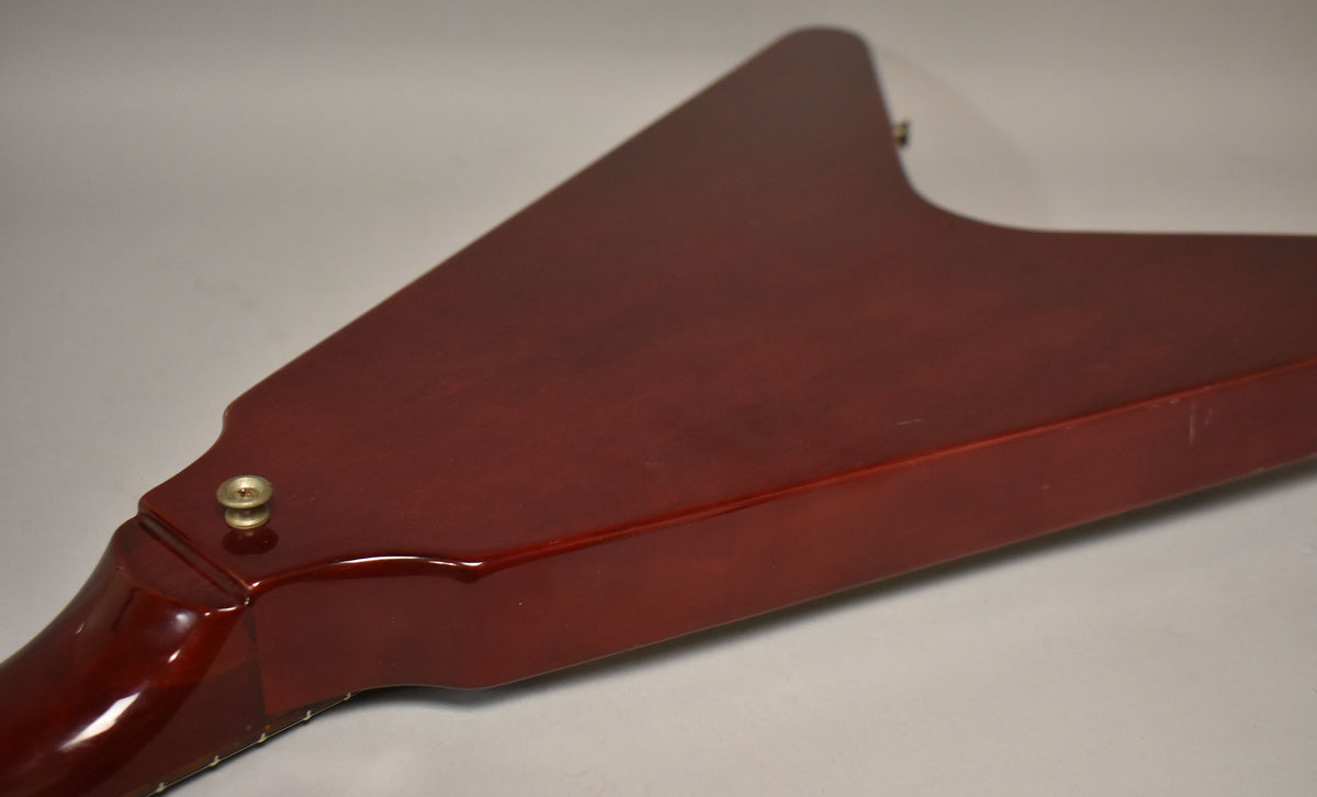 The back of a cherry red Flying V guitar, showing the neck joint and strap button, with minor scratches on the body.