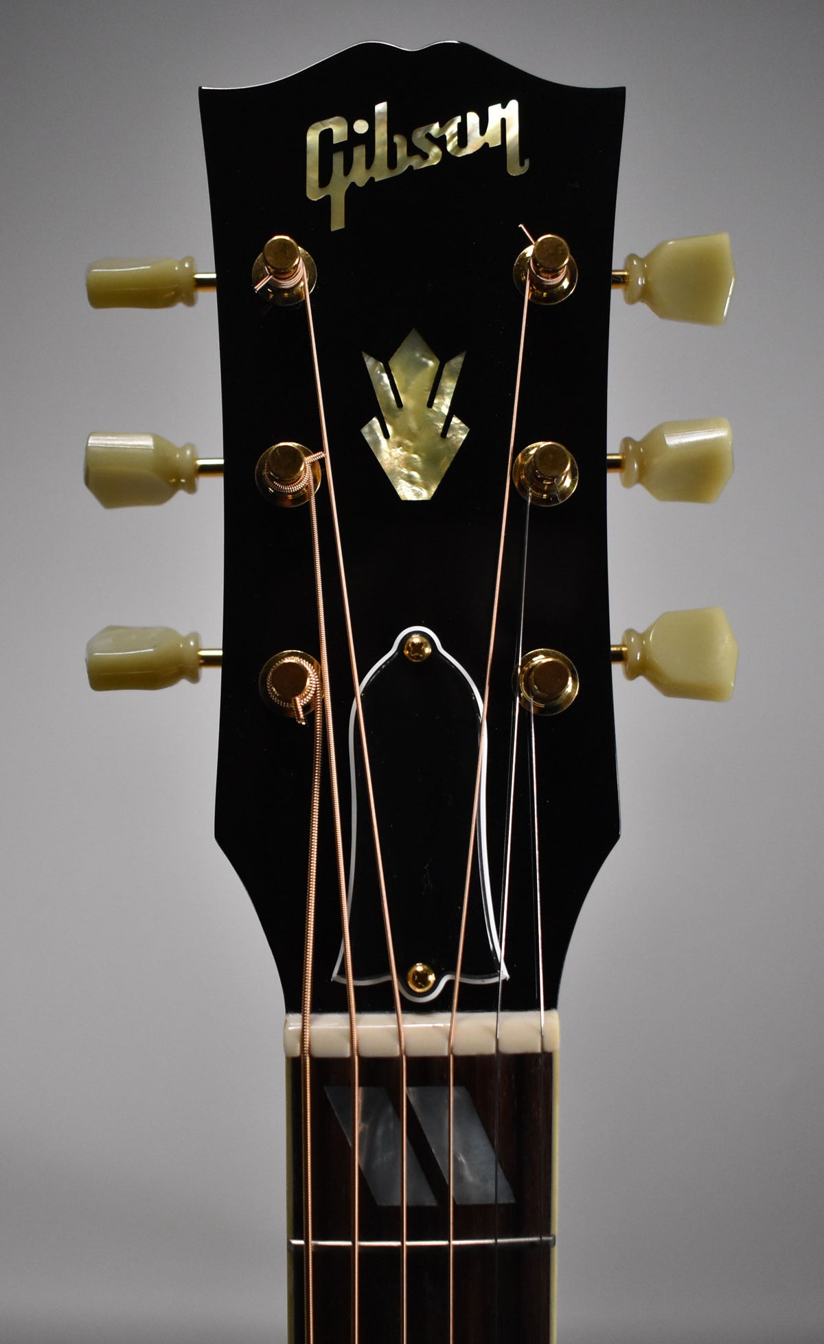 Close-up of the black headstock with mother-of-pearl inlay, gold tuners with cream buttons, and the top of the dark fretboard.