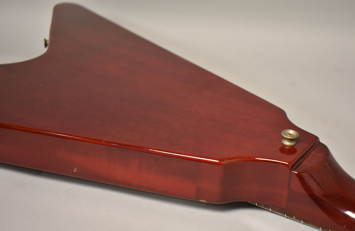 The cherry red Flying V body, viewed from the back, shows a glossy finish with some minor scuffs and a brass strap button near the neck joint.