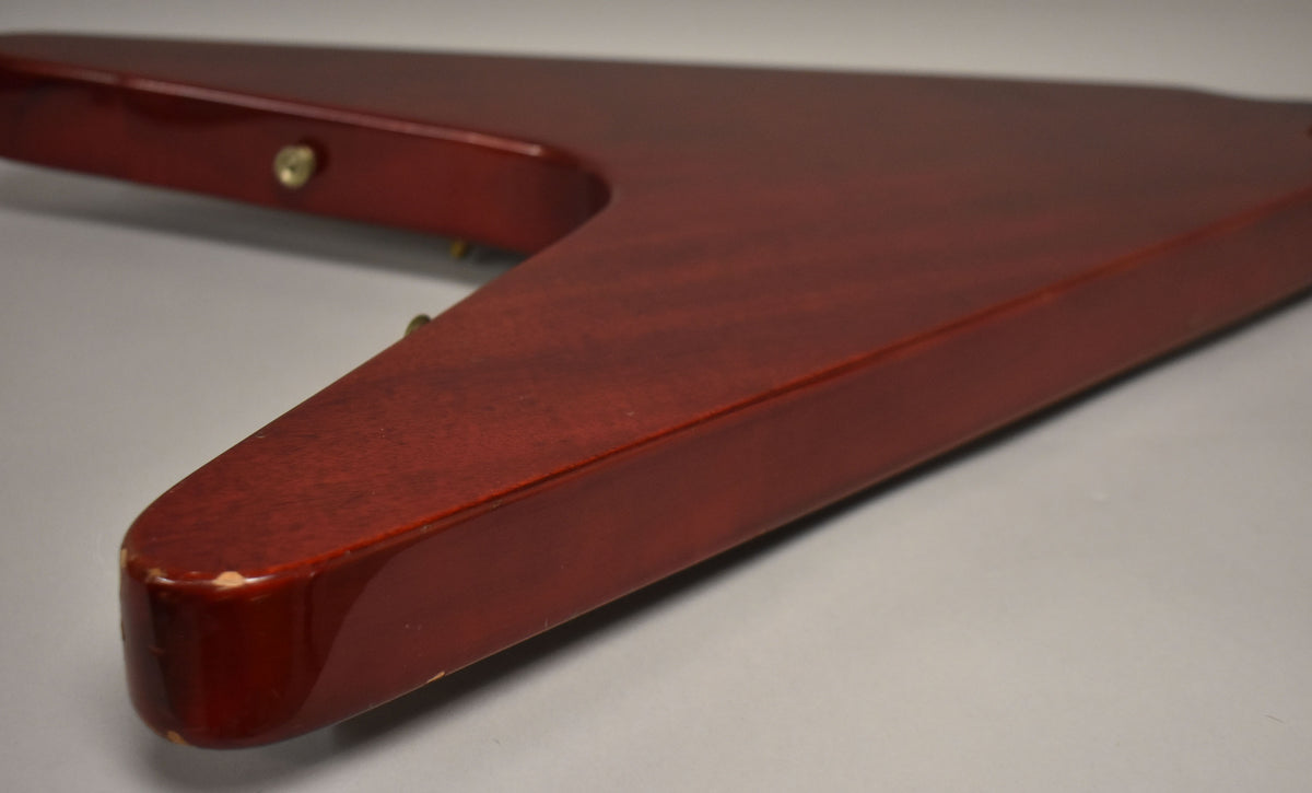 Close-up of the cherry red Flying V's lower wing, showing a worn corner with chipped finish and a visible wood grain.