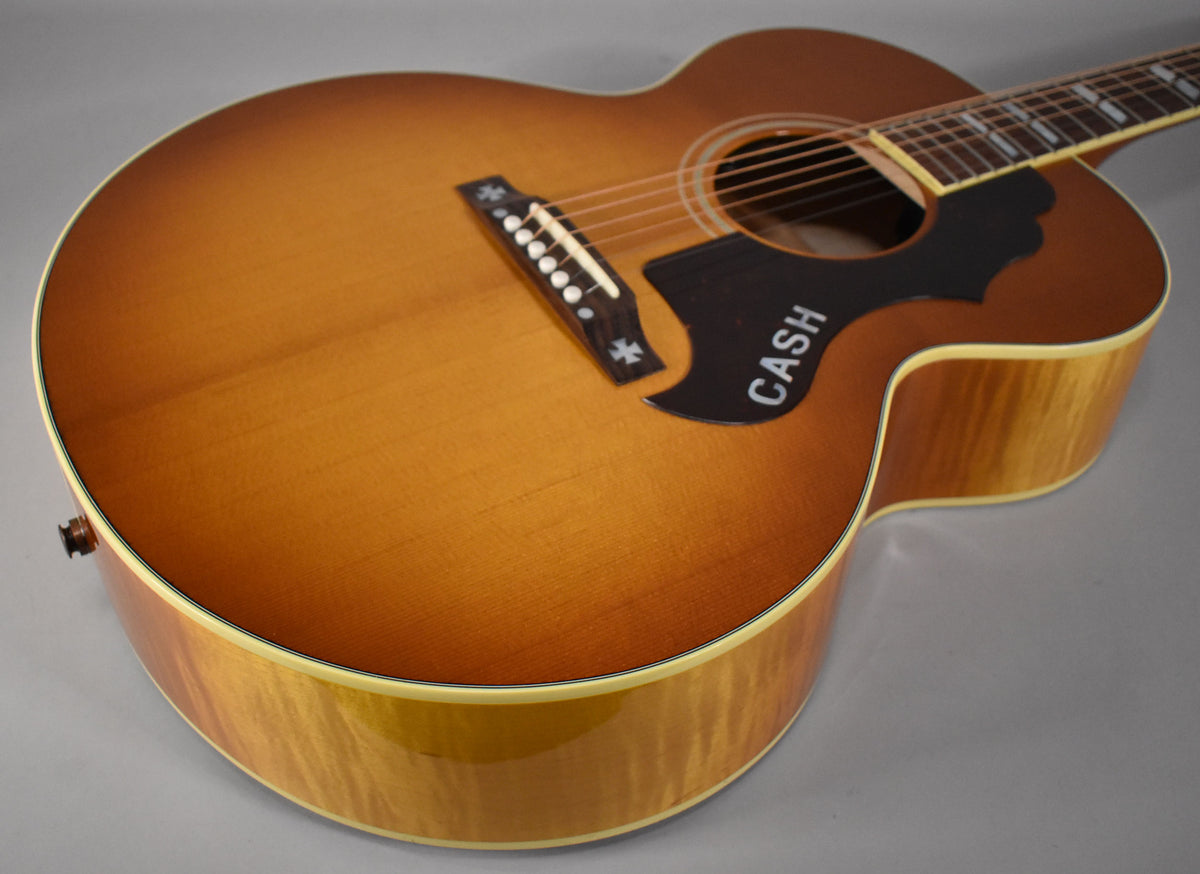 The acoustic guitar's cherry sunburst top and figured maple sides are visible from a high angle, with a "CASH" pickguard.