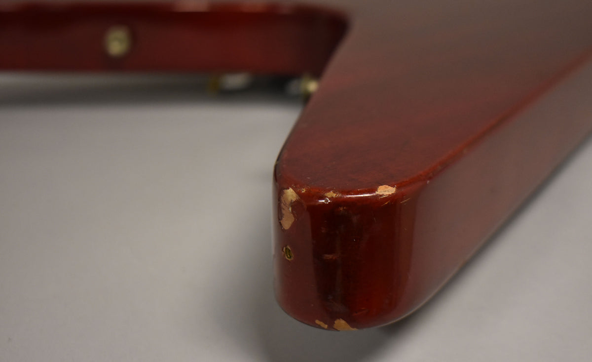 Close-up of the cherry red Flying V's lower wing tip, showing significant finish chips and wear along the edges.
