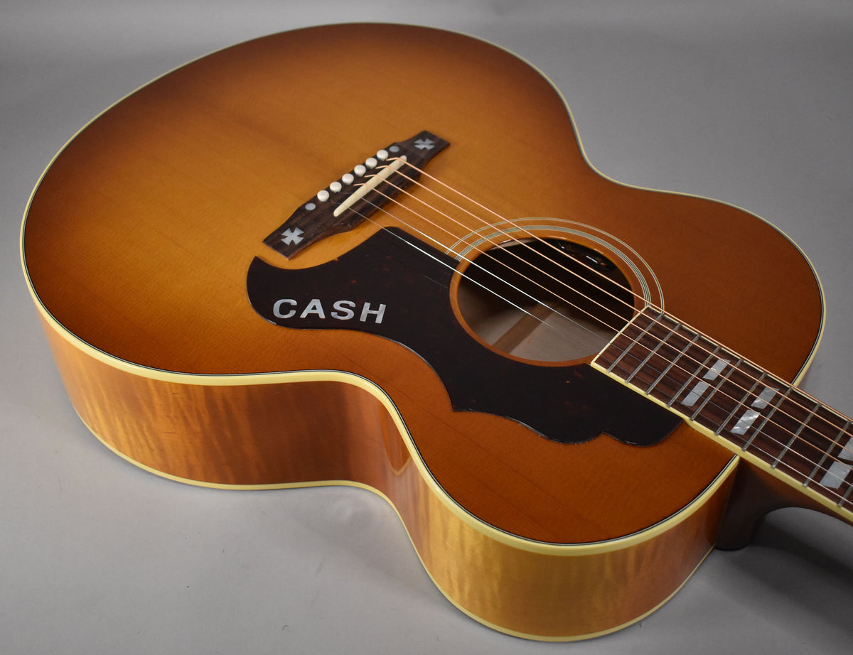 Acoustic guitar, angled view of the cherry sunburst body, showing the bridge with star inlays, black pickguard with "CASH", and neck with block inlays.