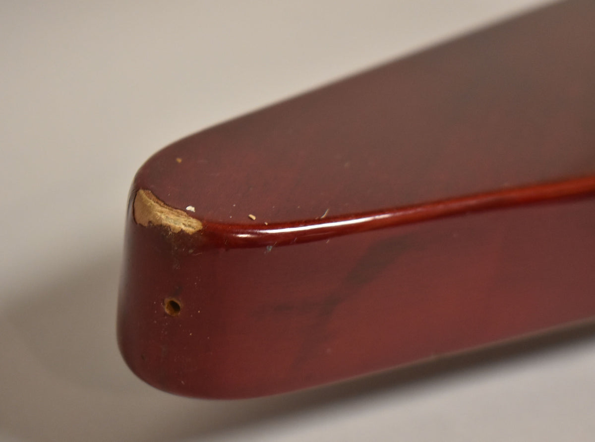 Close-up of the cherry red guitar body's lower bout, showing a large chip on the corner and a small screw hole on the side.
