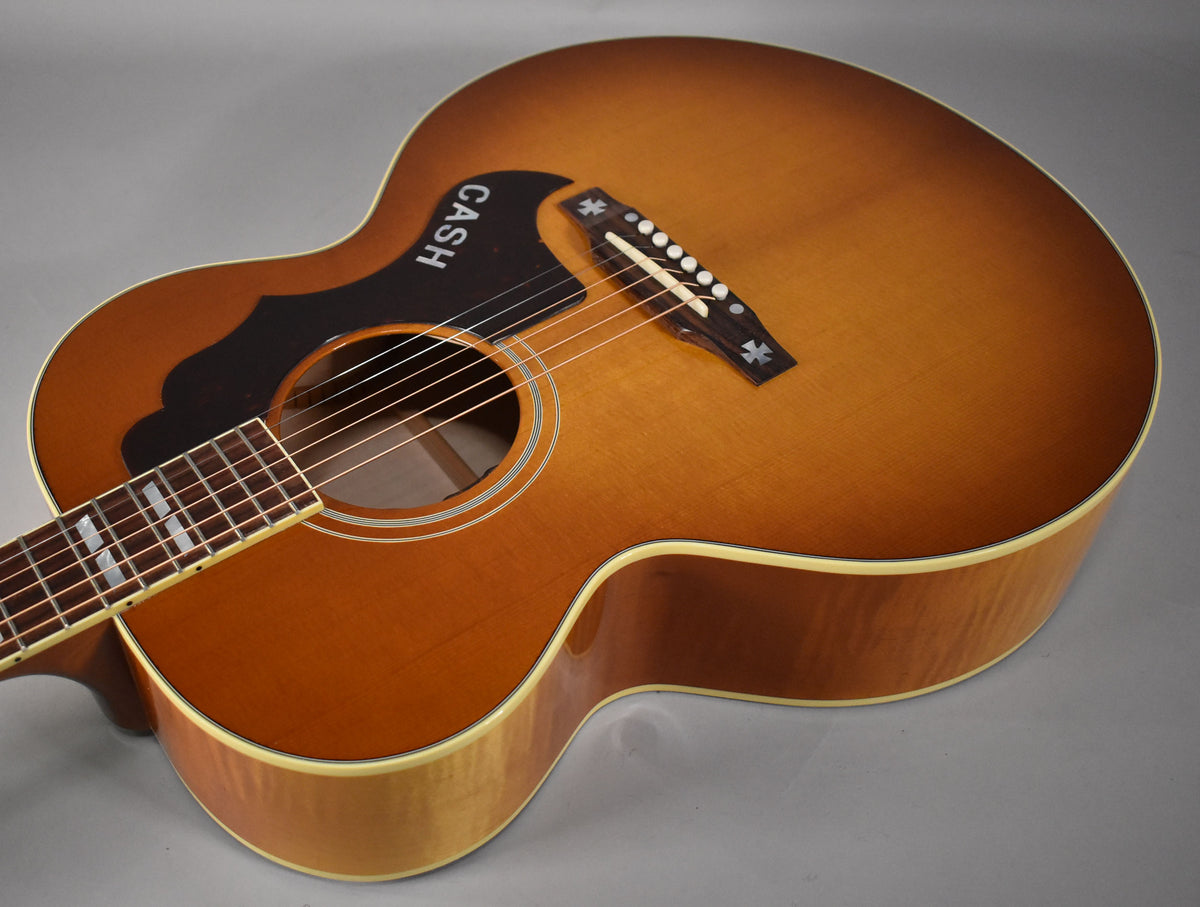 Acoustic guitar, cherry sunburst finish, angled view of the body and fretboard, with a black pickguard and "CASH" in white.
