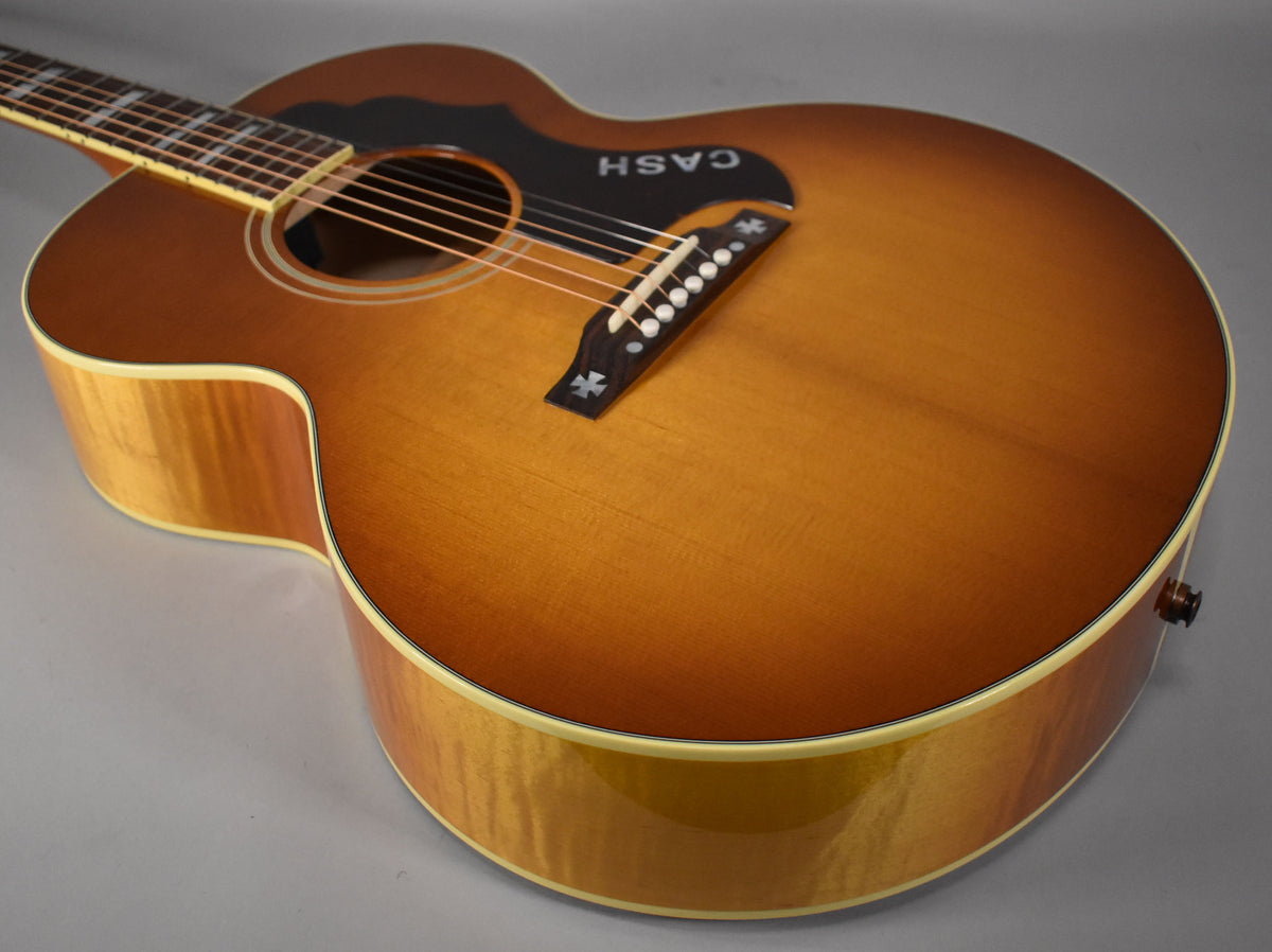 Acoustic guitar, angled from the upper bout, showing the cherry sunburst top, black pickguard, and light wood sides.