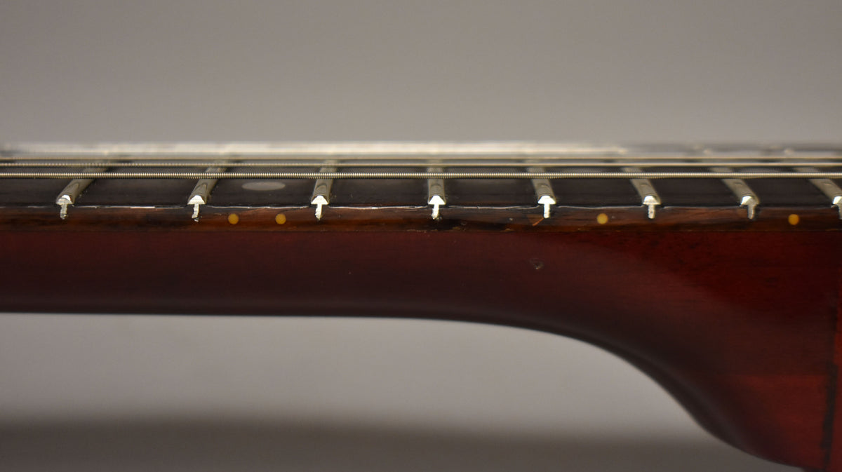 Close-up of the dark rosewood fretboard with dot inlays and wear along the binding, showing the guitar's strings and frets.