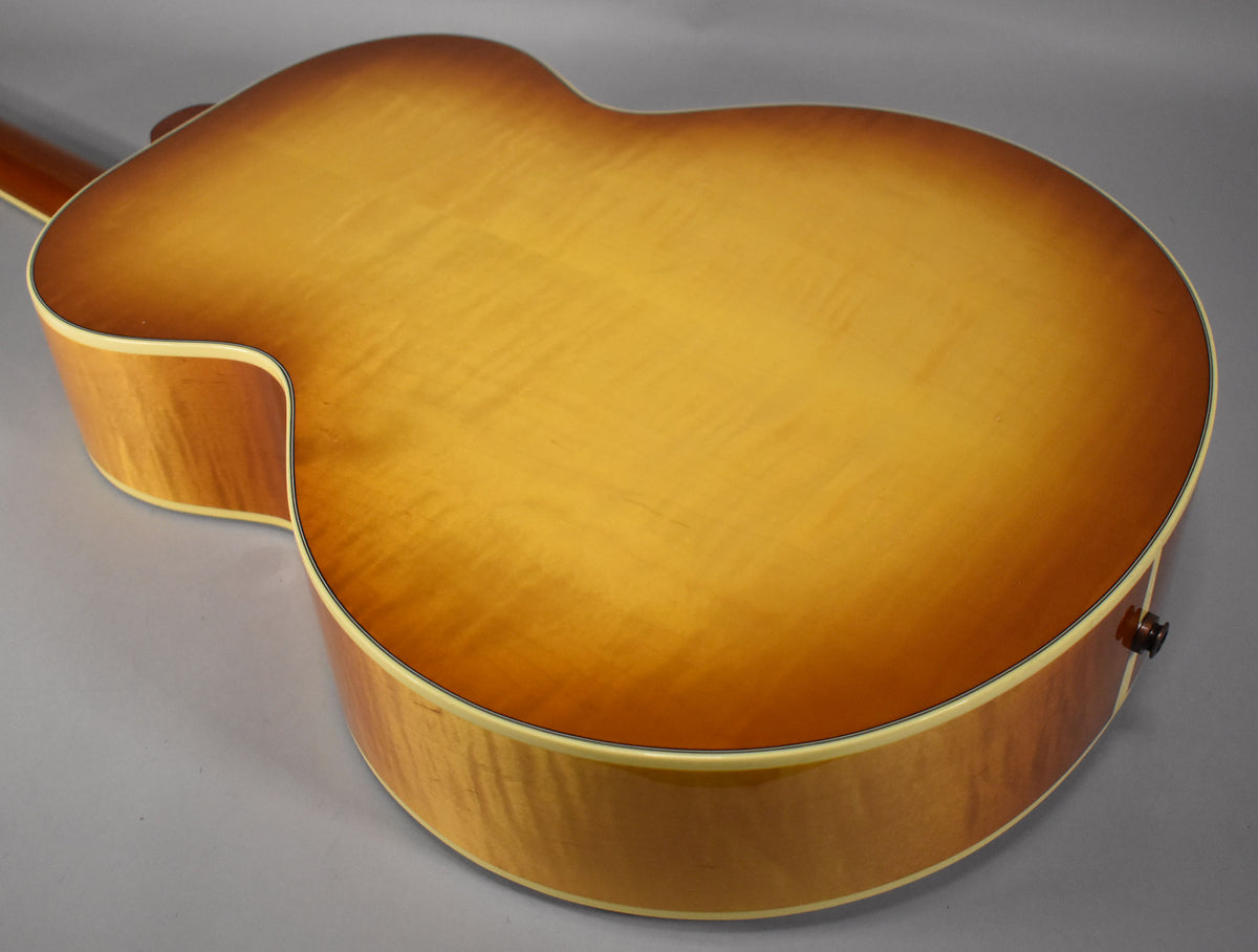The back of the acoustic guitar, showing a cherry sunburst finish with visible wood grain and a black endpin jack.
