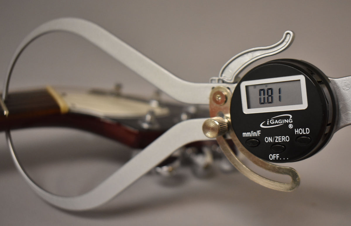 A digital caliper measures the guitar's neck relief at 0.81, with the headstock and tuners blurred in the background.
