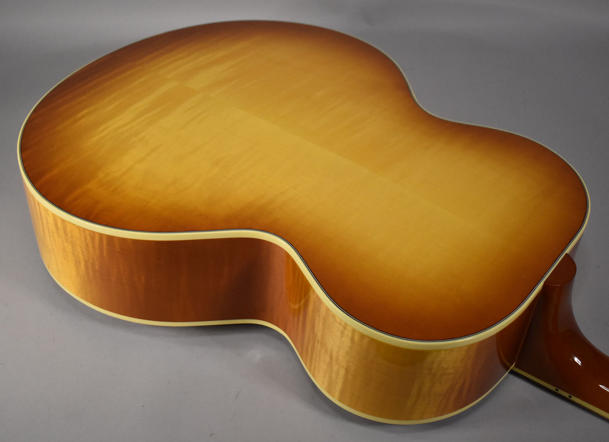 The back of the acoustic guitar, angled from the upper bout, shows a cherry sunburst finish with flame maple grain and cream binding.