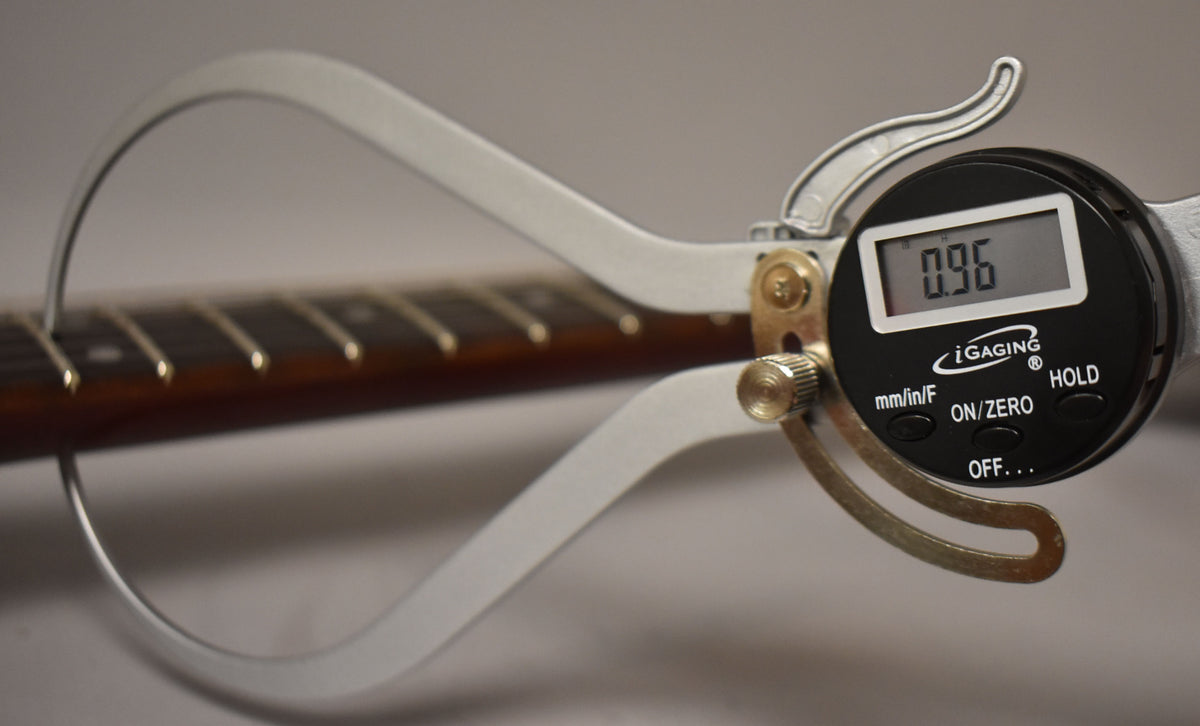 A digital caliper measures the fret height at 0.96mm on the guitar's dark brown fretboard with shiny metal frets.