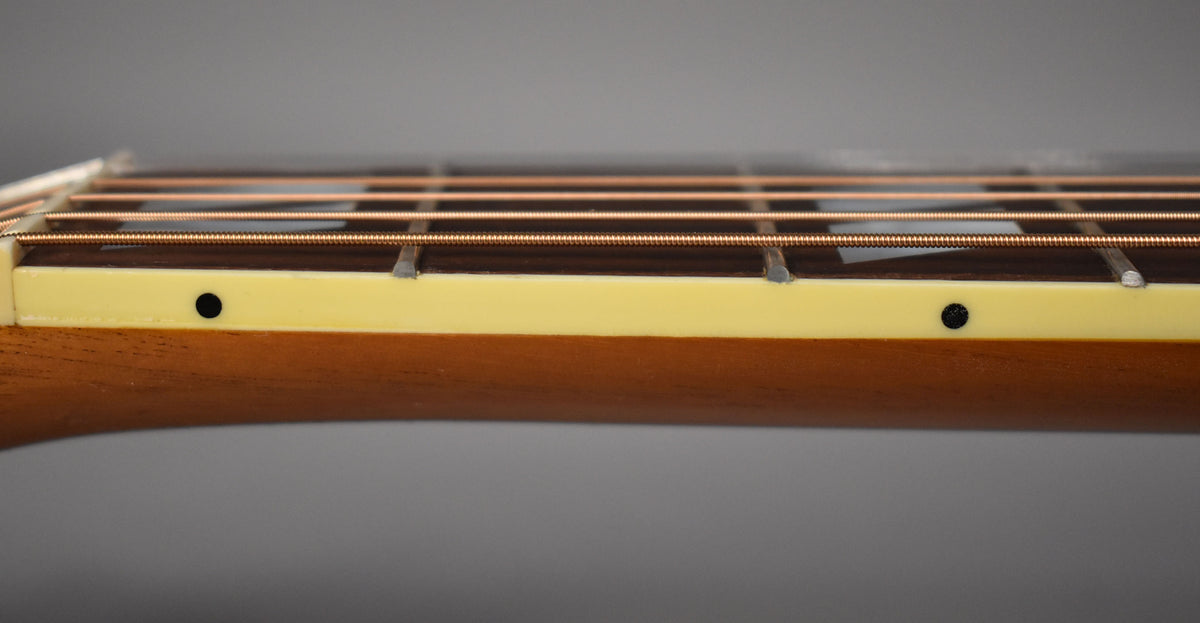 Close-up of the guitar's fretboard from the side, showing the light cream binding with two black dot side markers and bronze strings.