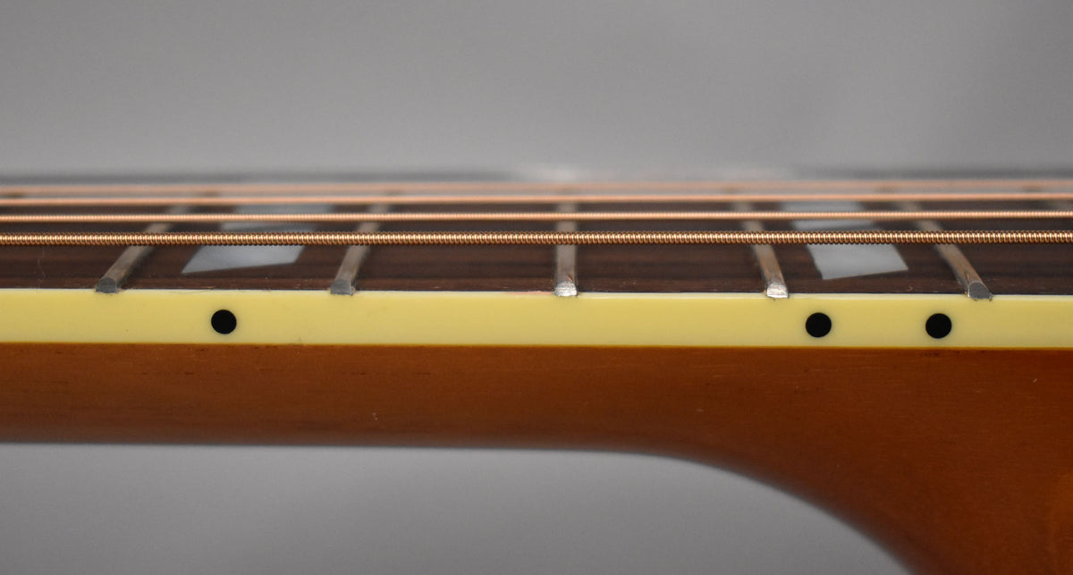 Close-up of the guitar's neck, showing the dark fretboard with trapezoid inlays, light binding, and side dot markers.